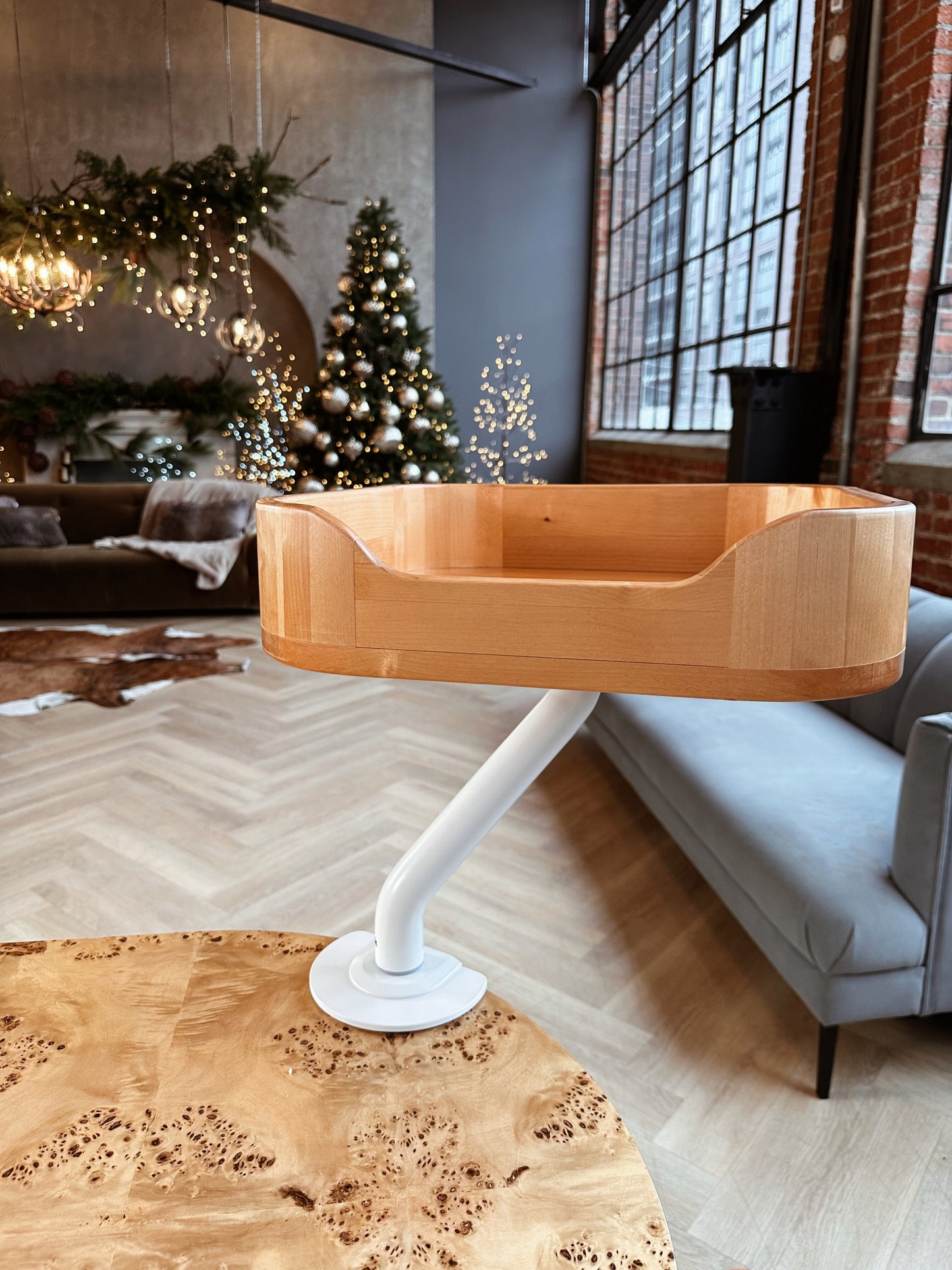 Close-up of an empty wooden ERGO PURRCH™ desk-mounted cat bed with a white arm, in a holiday-themed loft with festive decor, Christmas tree, and cozy lighting.